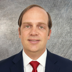 Professional headshot of a man in a navy suit and red tie, against a gray textured backdrop.