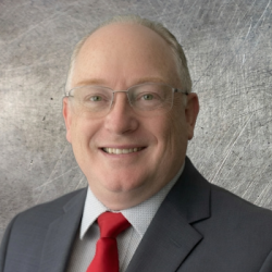Professional headshot of a smiling man in a dark suit, white shirt, and red tie, wearing glasses against a gray textured backdrop.