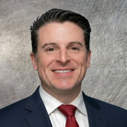 Smiling man in a navy suit and red tie poses for a professional headshot against a textured gray background.